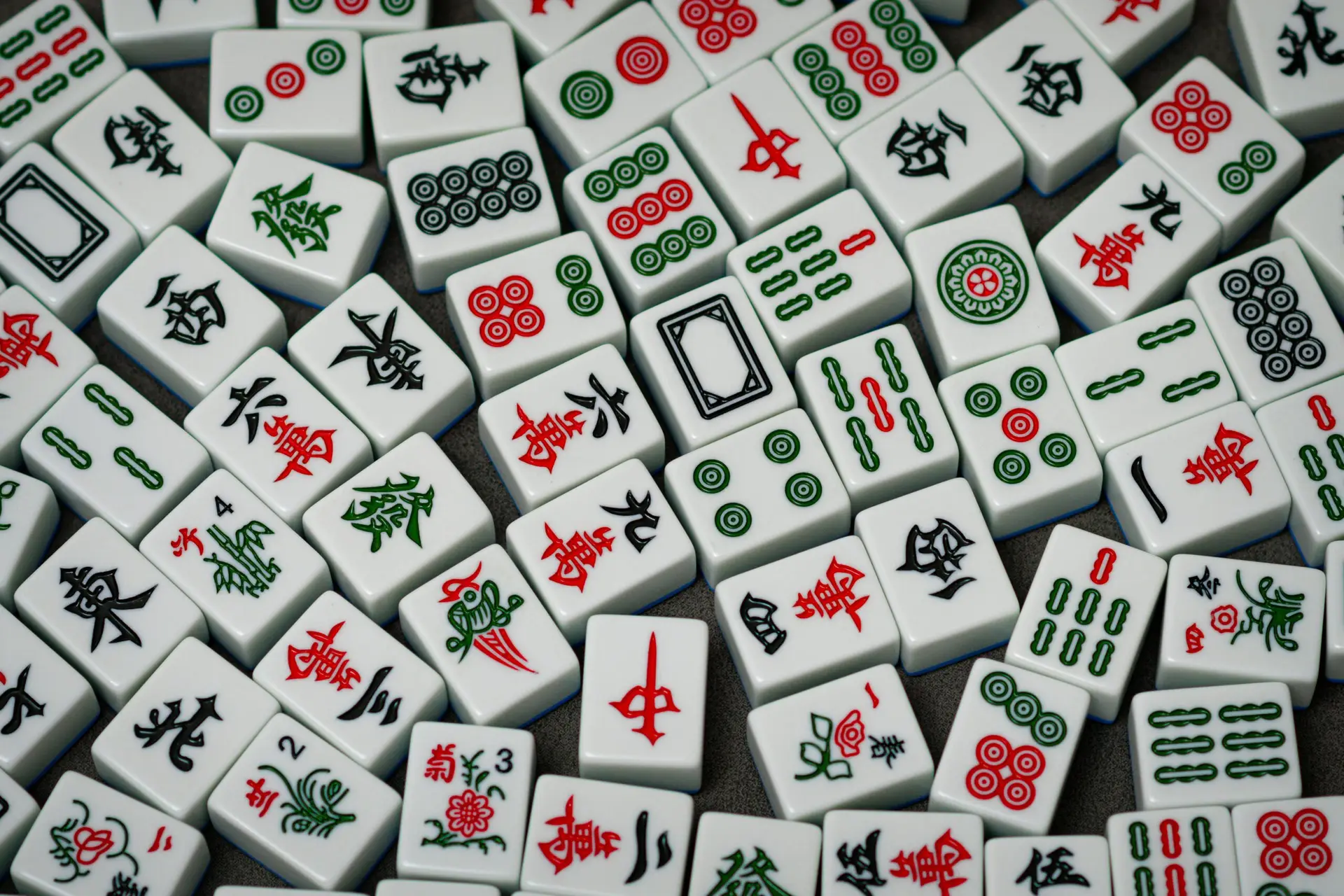 Scattered Mahjong tiles displaying various traditional patterns, characters, and symbols in green, red, and black.