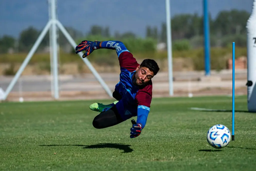 A goalkeeper diving quickly to stop a ball during training, demonstrating athletic reaction time and rapid reflex movement.