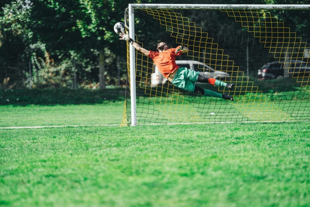 Goalkeeper leaping to save a soccer ball during an outdoor match.